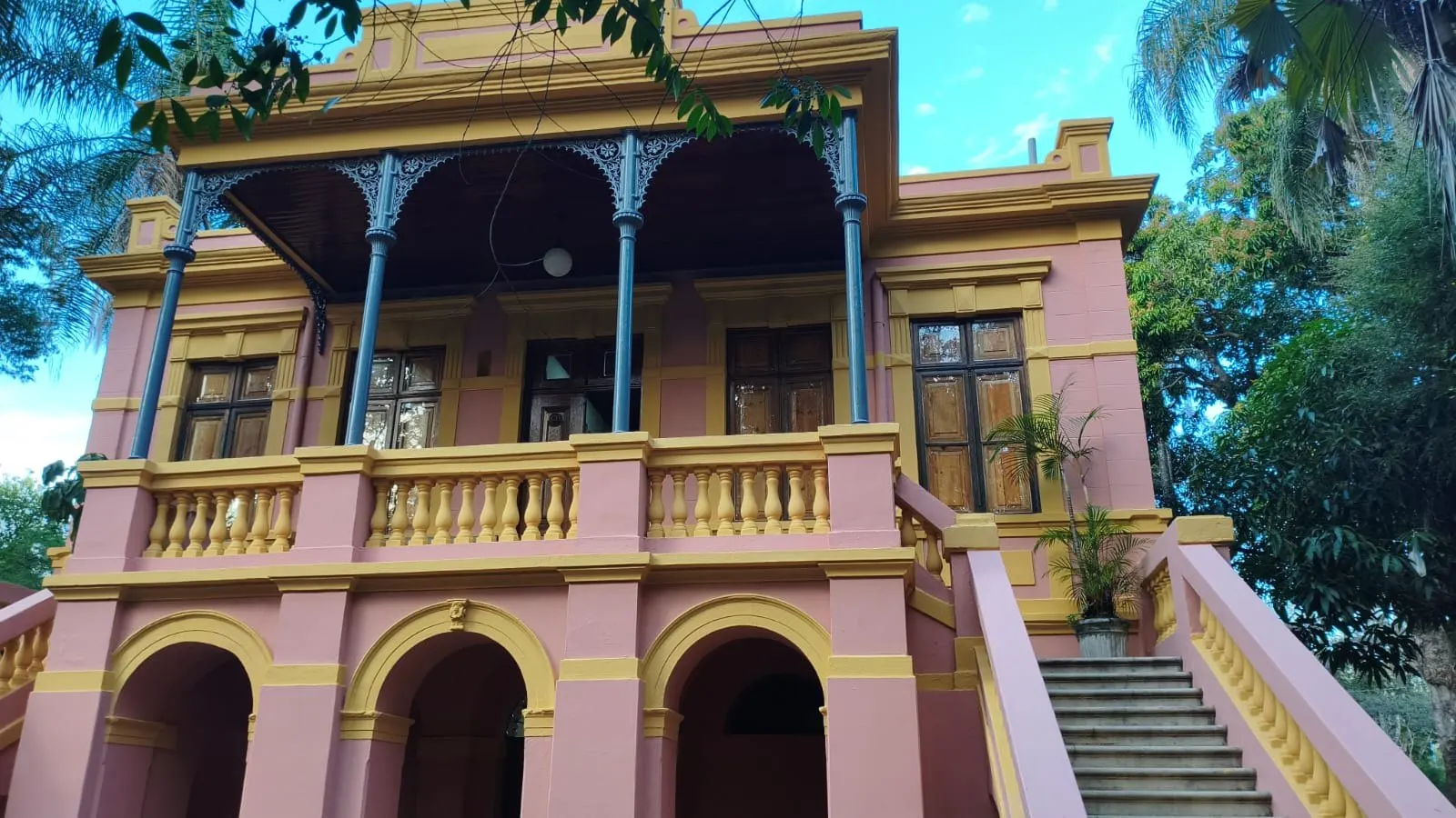 Varanda frontal do Palacete Ferraz Costa com arcos e colunas de ferro, em rosa e amarelo
