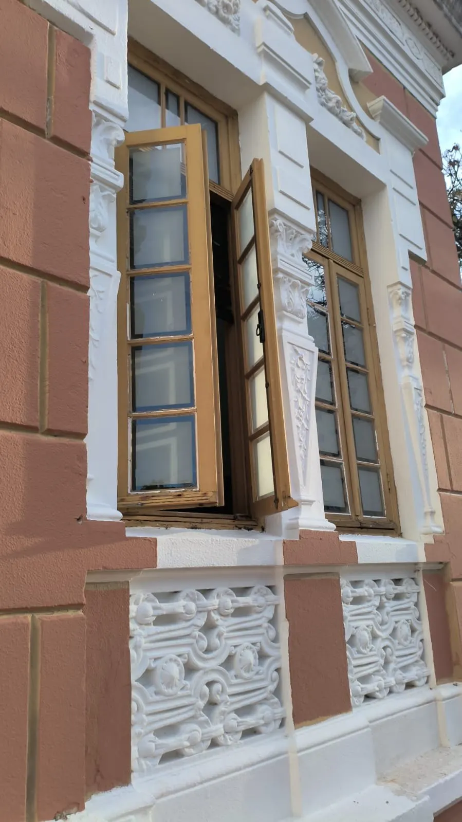 Janela com moldura ornamentada pintada em branco sobre parede terracota