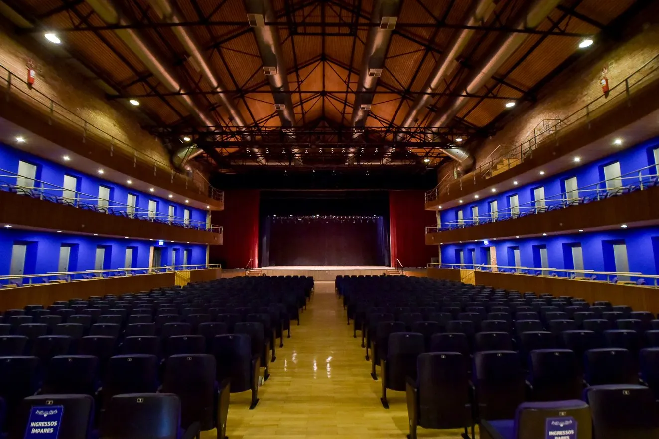 Vista da plateia para o palco do Teatro Polytheama com cortina vermelha