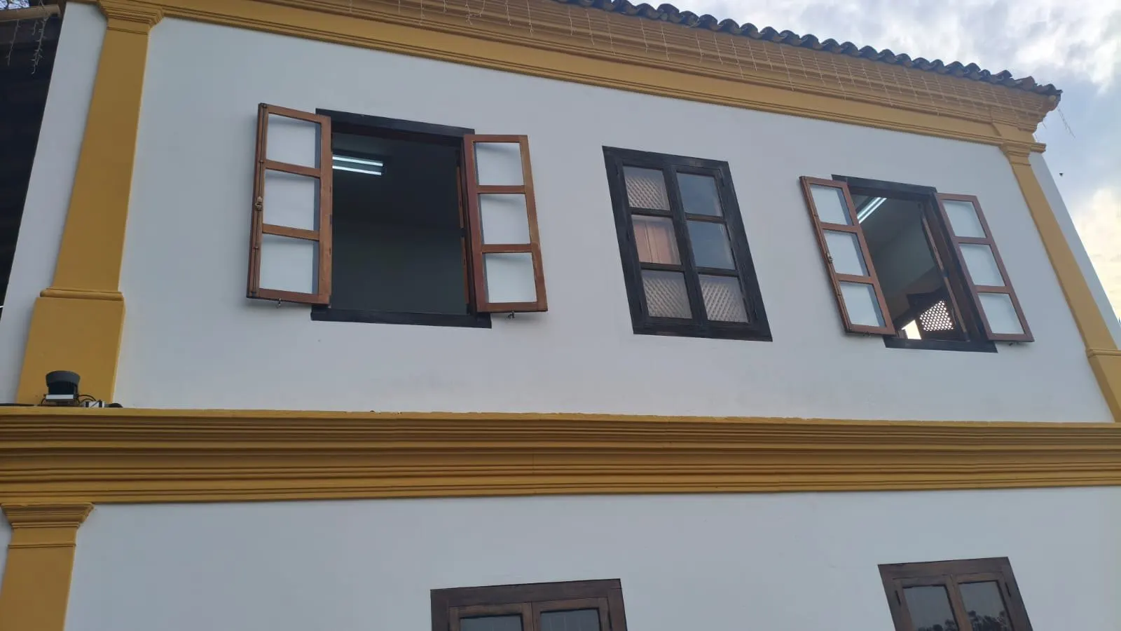 Detalhe de janelas com venezianas de madeira sob a cimalha amarela