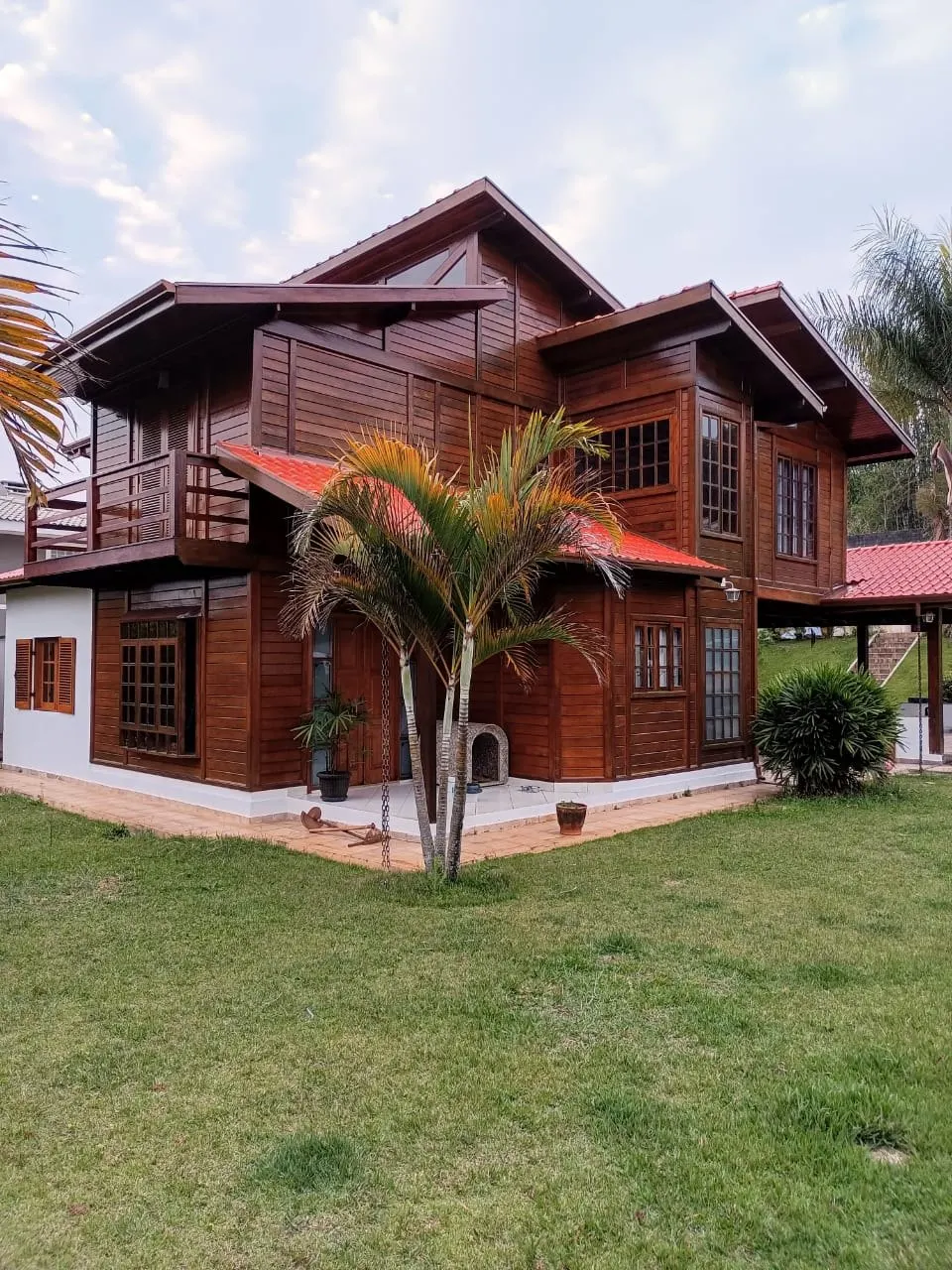 Casa de campo em madeira vista do gramado com palmeira