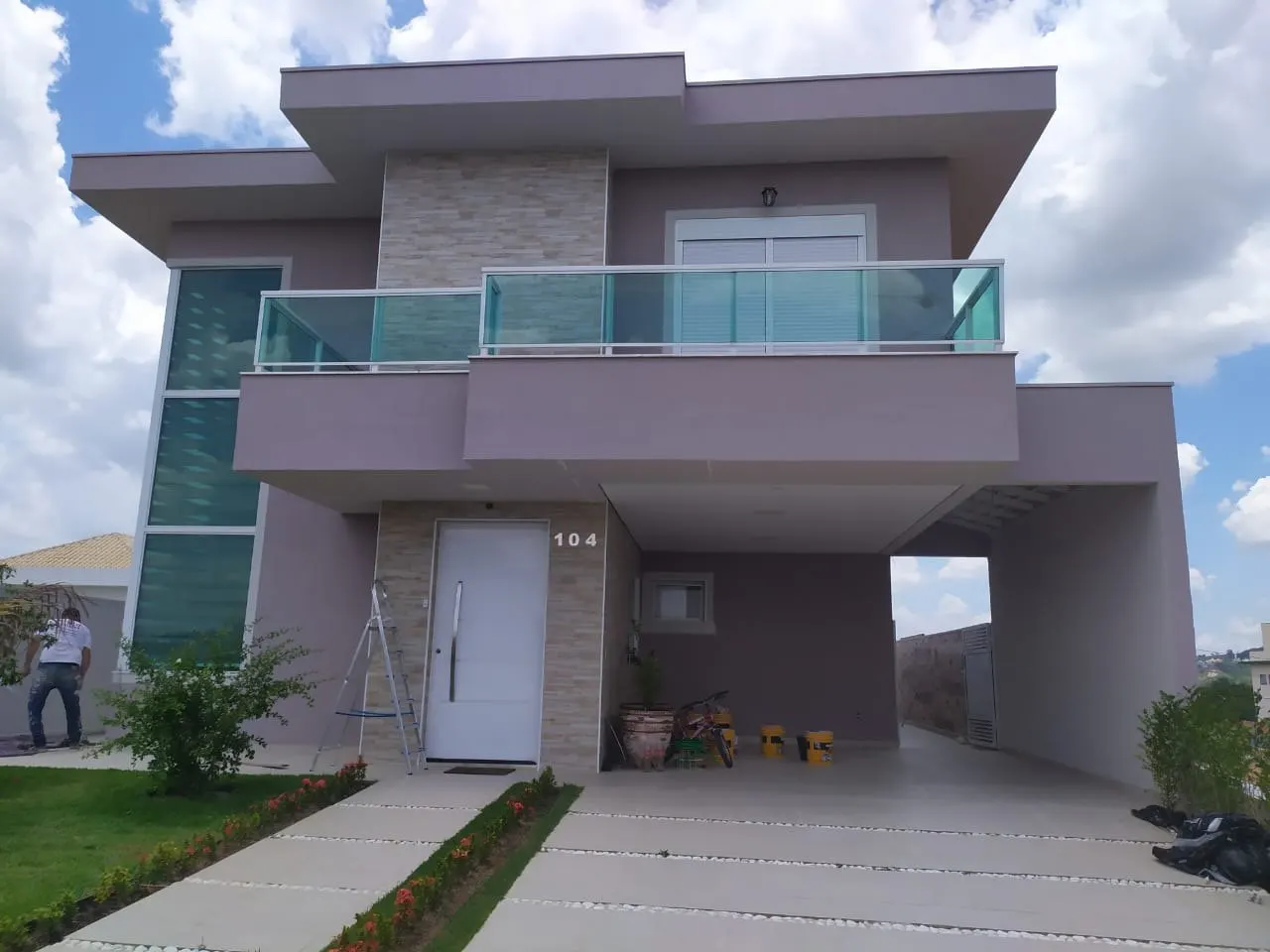 Fachada frontal de sobrado repintada, com pintor finalizando a garagem