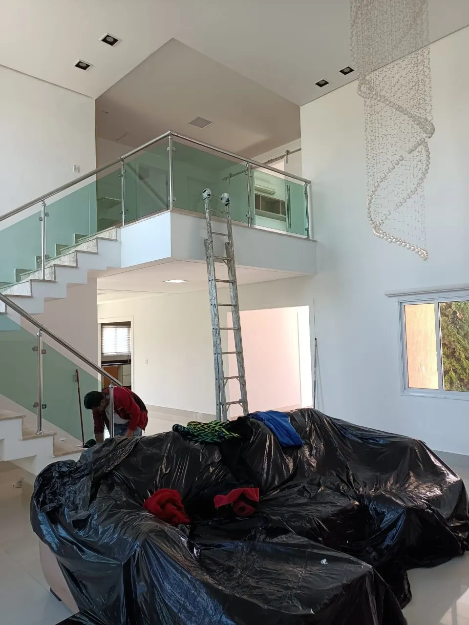 Pintor em escada no pé-direito duplo, com móveis cobertos por lona