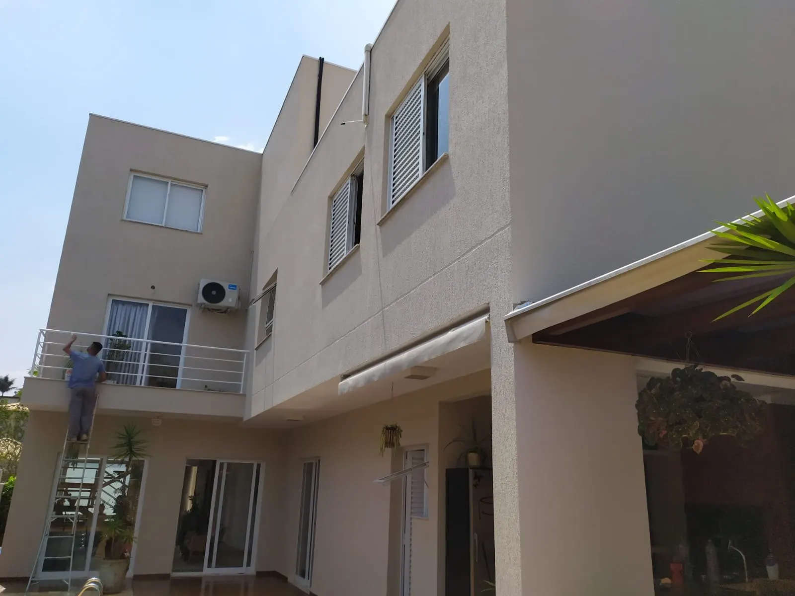 Pintor em escada pintando a fachada lateral de um sobrado